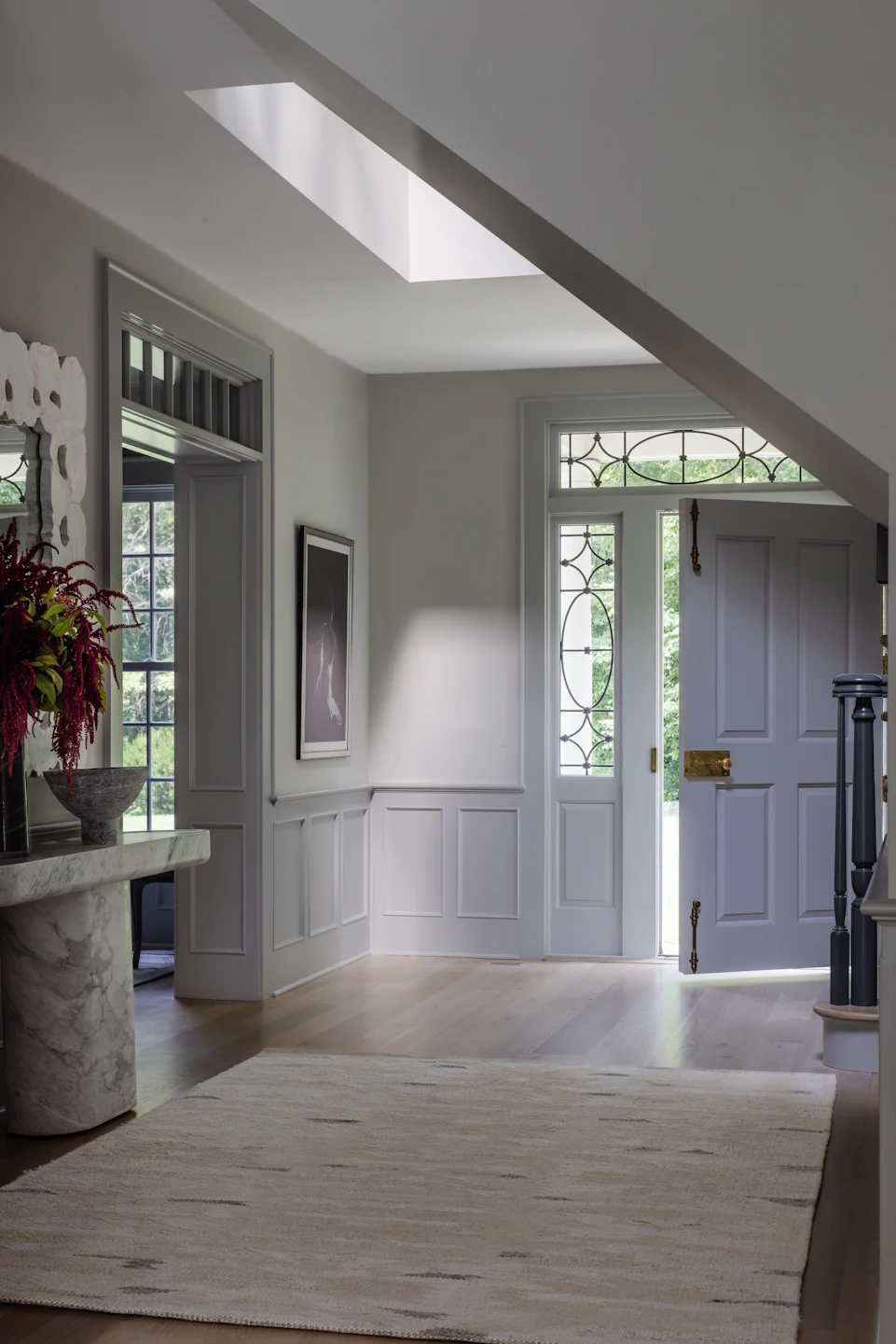Classic colonial entry foyer with skylight, white paneled wainscoting, marble console table, and leaded-glass front door in the Fairfield Transitional home
