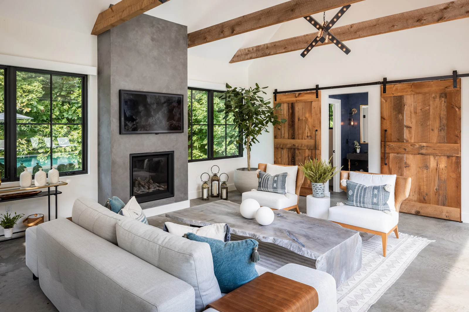 Pool house great room with concrete fireplace, mounted television, reclaimed barn doors, and vaulted ceiling at the Fairfield Transitional project