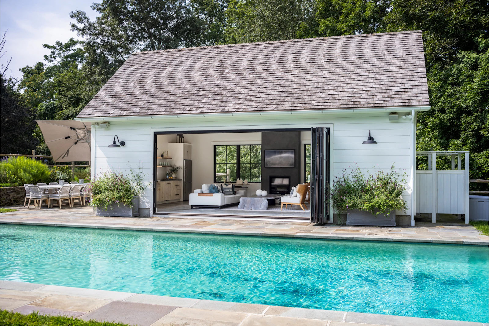 Custom pool house with bifold glass doors opening to in-ground pool and bluestone patio at the Fairfield Transitional project in Fairfield, CT