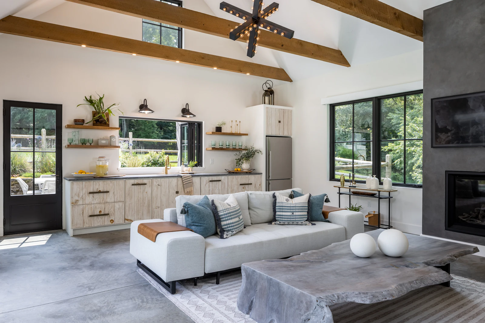 Pool house interior with vaulted ceiling, exposed wood beams, whitewashed kitchenette, and concrete floors in the Fairfield Transitional home